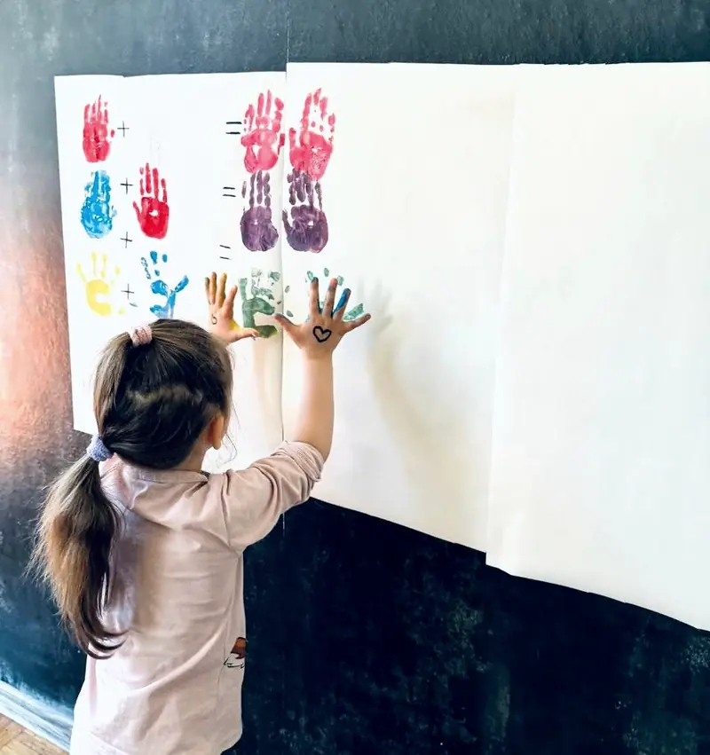 Dziewczynka odciska pomalowane dłonie na dużym arkuszu papieru