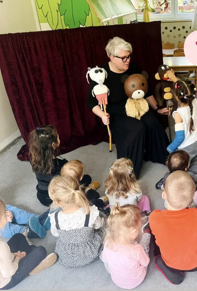 Język i komunikacja: Dzieci siedzą na dywanie i oglądają teatrzyk z pacynkami